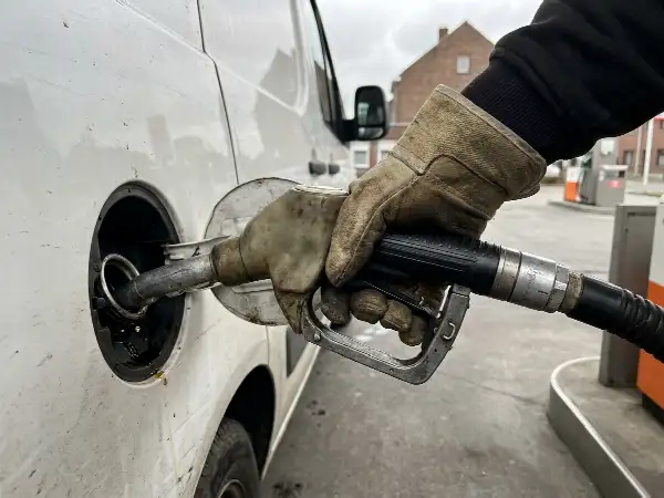 Hand met werkhandschoen houdt het vulpistool in de tankopening van een bestelwagen